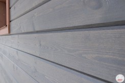 На фасаде блок-хаус брус с тонкопиленой поверхностью, покрытый лессирующим составом Teknos. Хвоя 25*192(172) мм, цвет ТМ 1835 (серый)